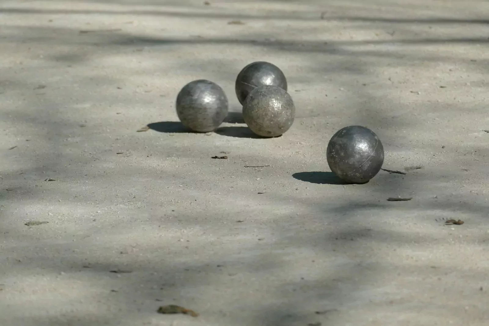 Four metal boules on a light-colored sandy surface with long shadows